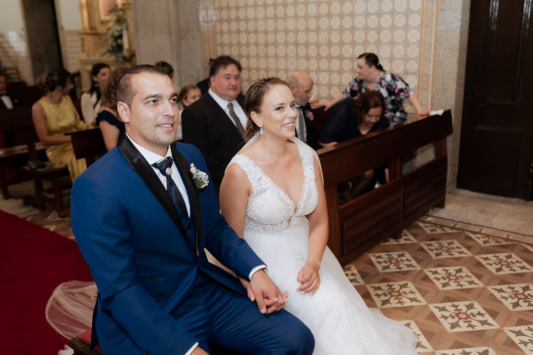 A couple in formal wedding attire sits in a church pew during their marriage ceremony.