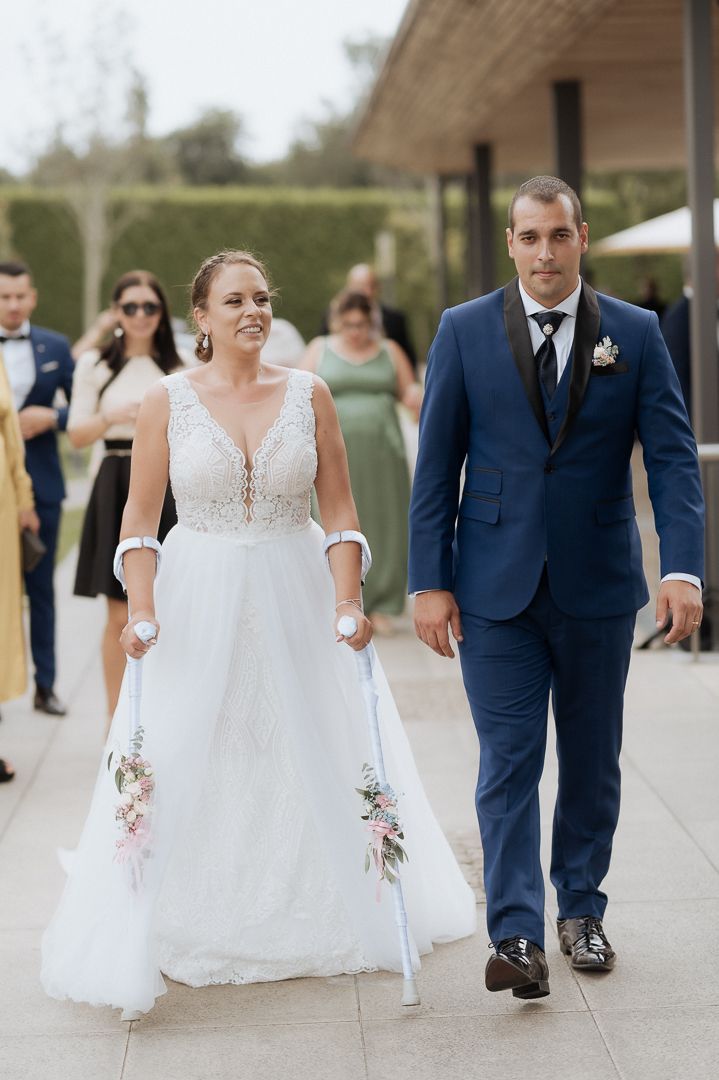 Couple walks together at outdoor wedding venue with bride wearing white lace dress and groom in navy blue suit.