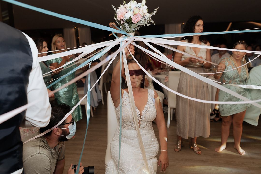 Wedding guests gather around blue and white ribbons streaming from a bouquet during a wedding reception celebration.