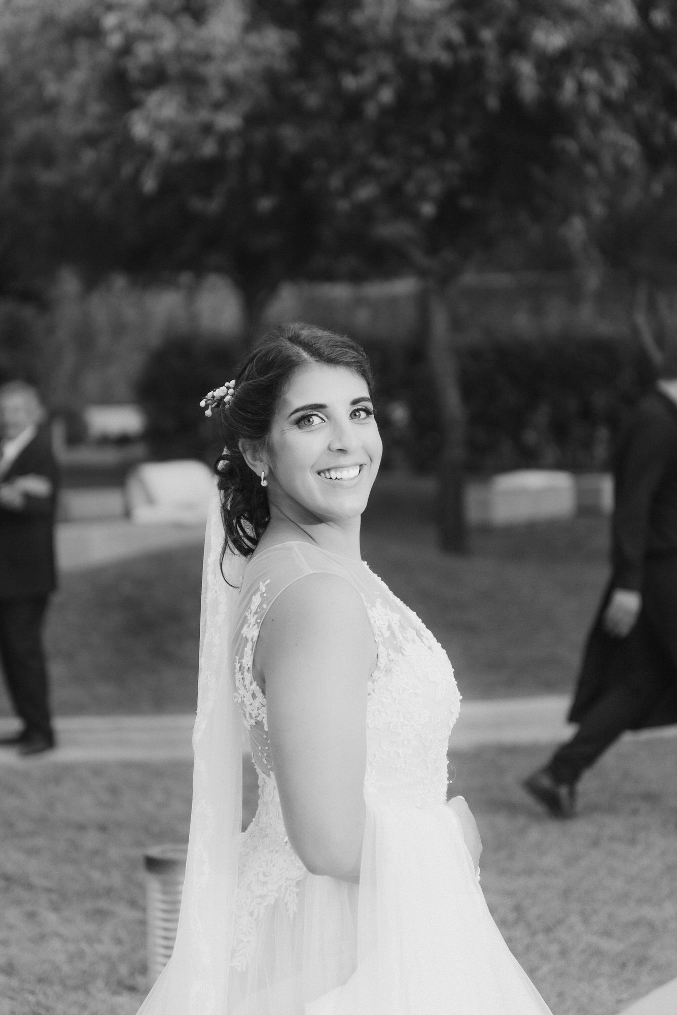 A black and white wedding portrait series of a bride in a white dress with veil posing outdoors in a garden setting.