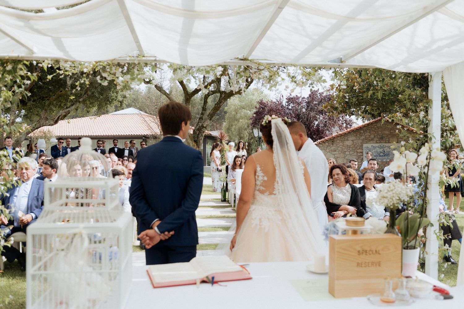 An outdoor wedding ceremony under a white tent canopy with decorative jars and floral arrangements.