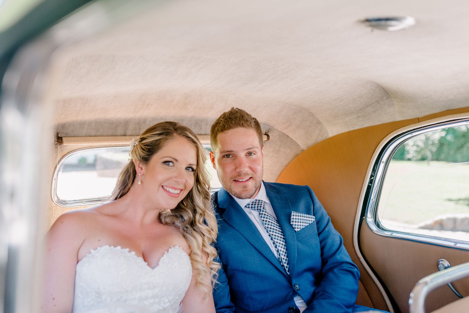 Recém-casados sorriem sentados no banco de trás de um carro antigo. Fotografia de Casamento