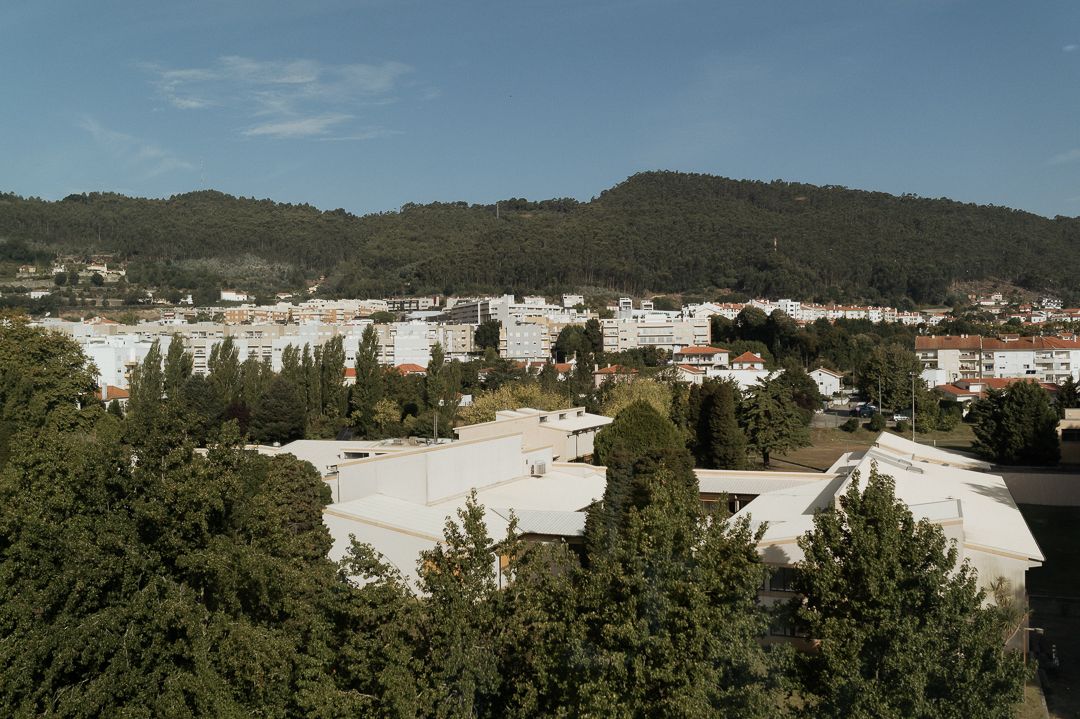 Elevated view of a suburban area with white buildings and pine trees against a backdrop of forested hills.