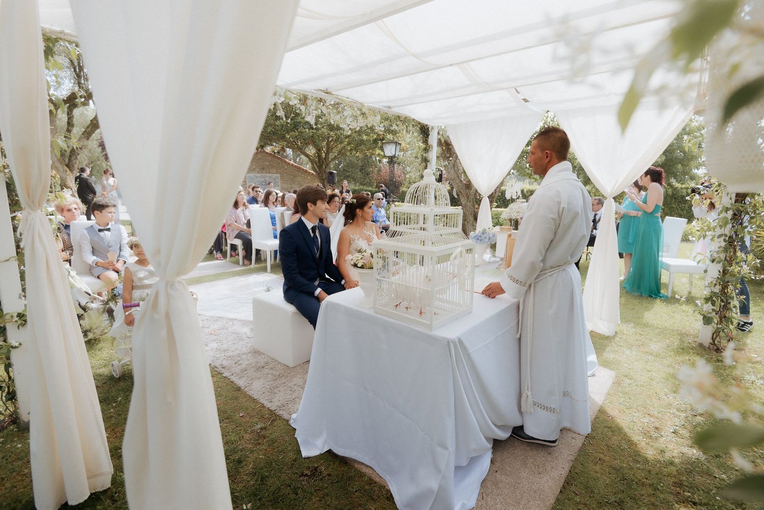 White draped fabric creates elegant archways over outdoor seating at an elegant garden wedding reception setup.