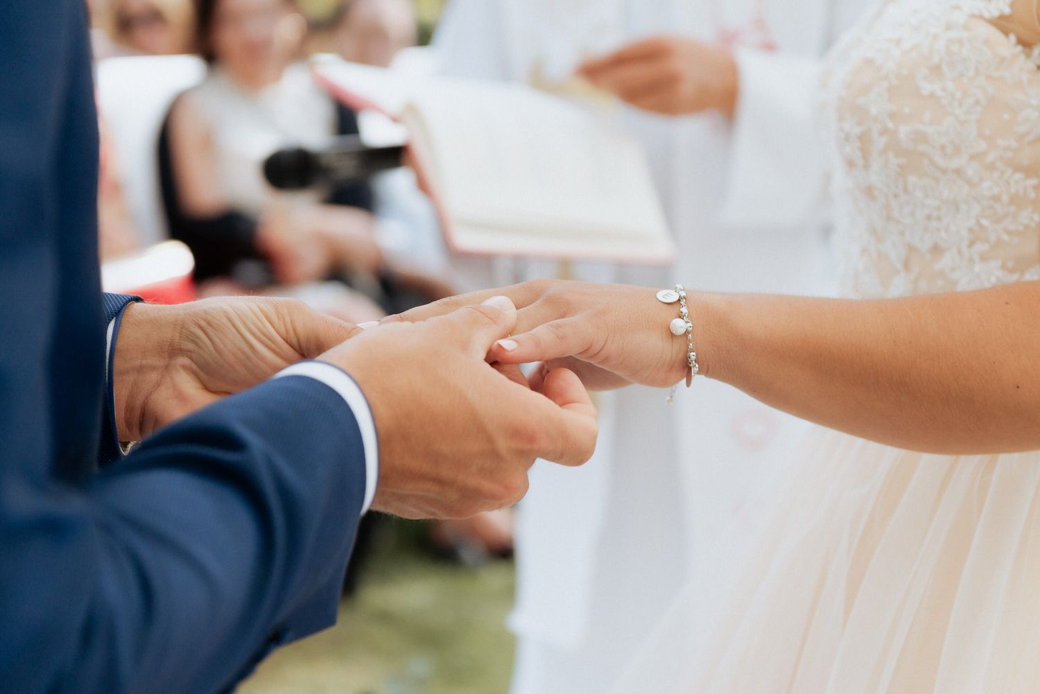 Close up of bride and groom exchanging rings during wedding ceremony, with bride wearing white dress and bracelet.