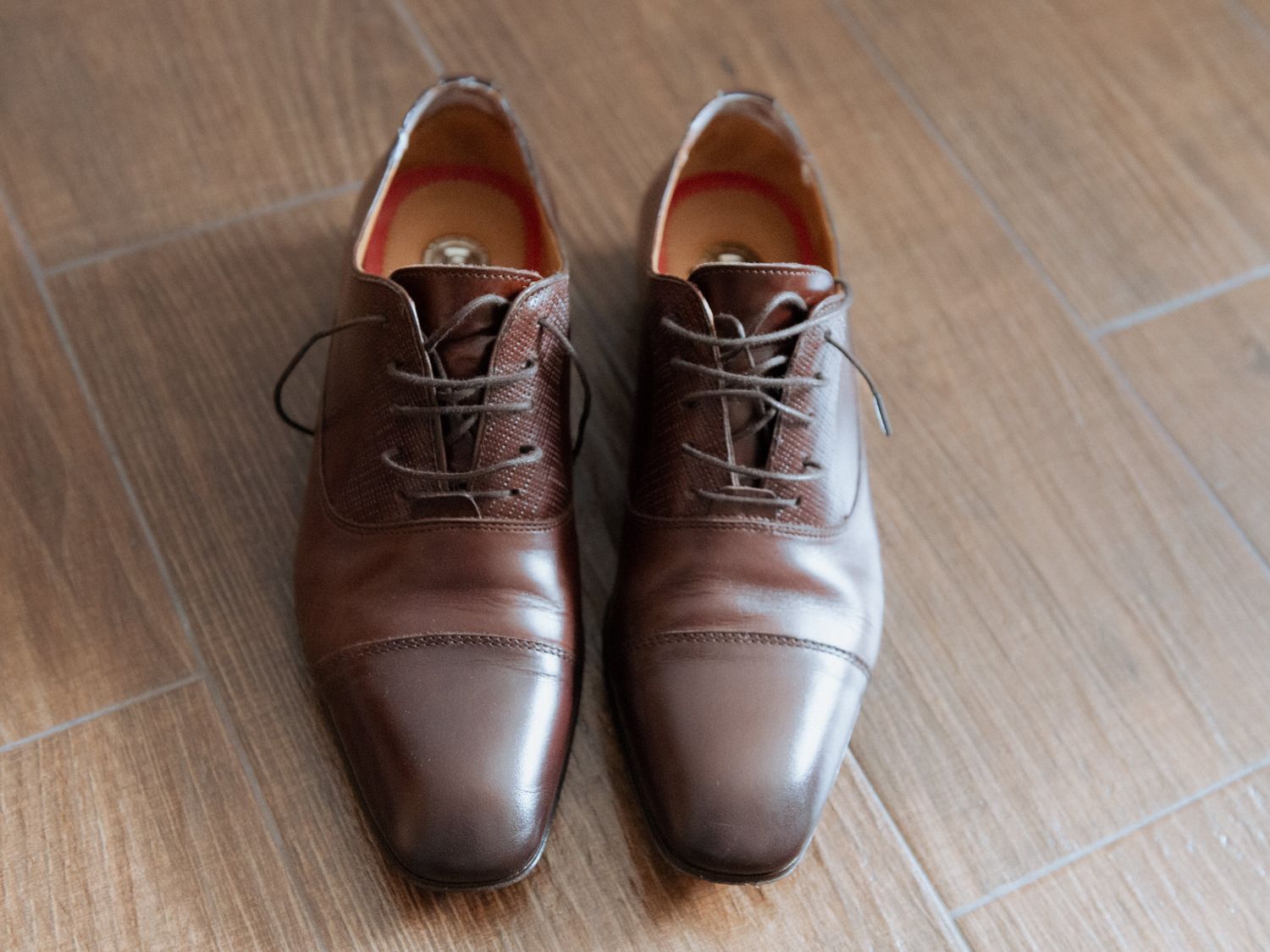 Seven sequential photos show the lacing progression of brown leather oxford dress shoes on a wooden floor.