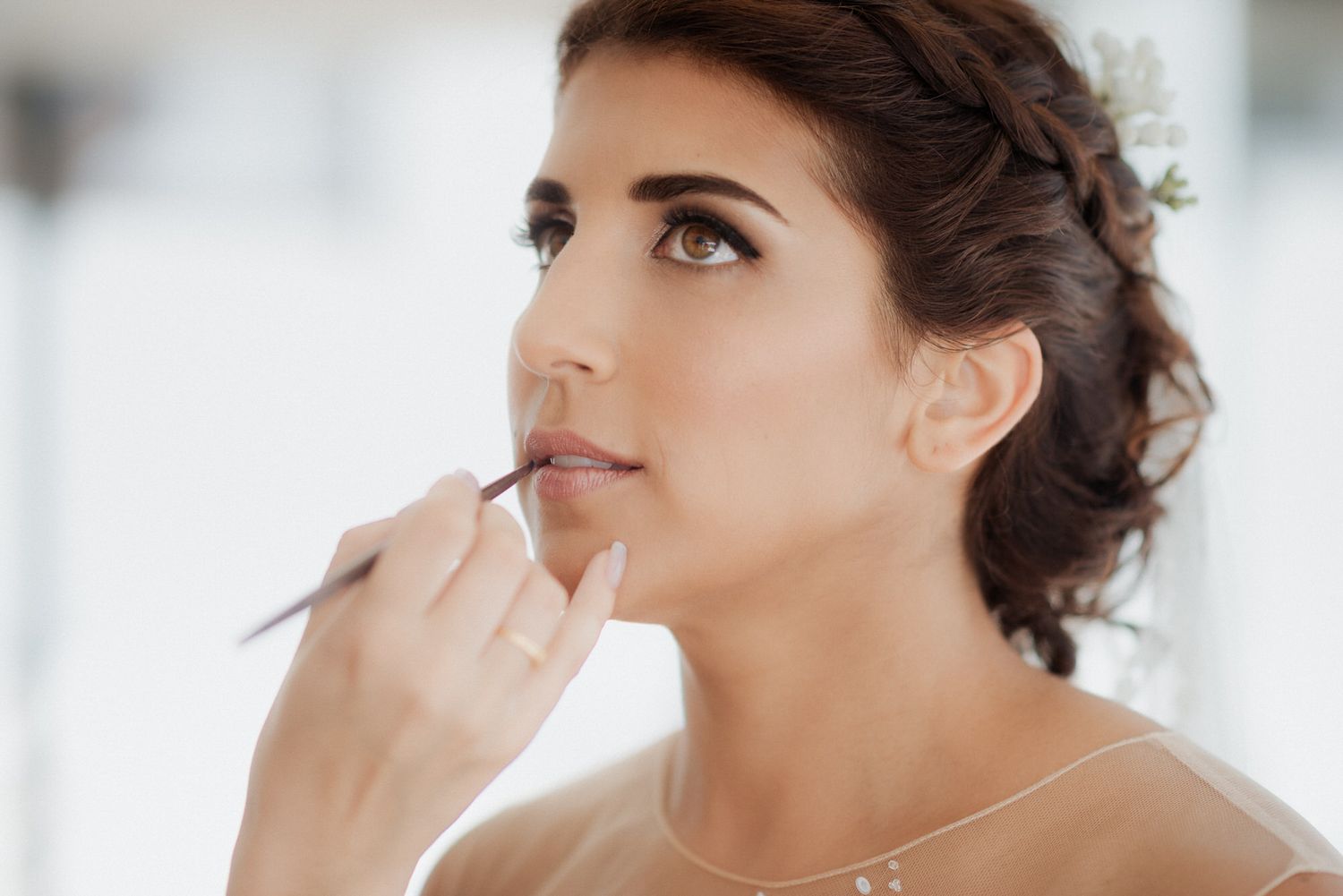 A bride receiving professional makeup application during wedding preparation in a bright white room.