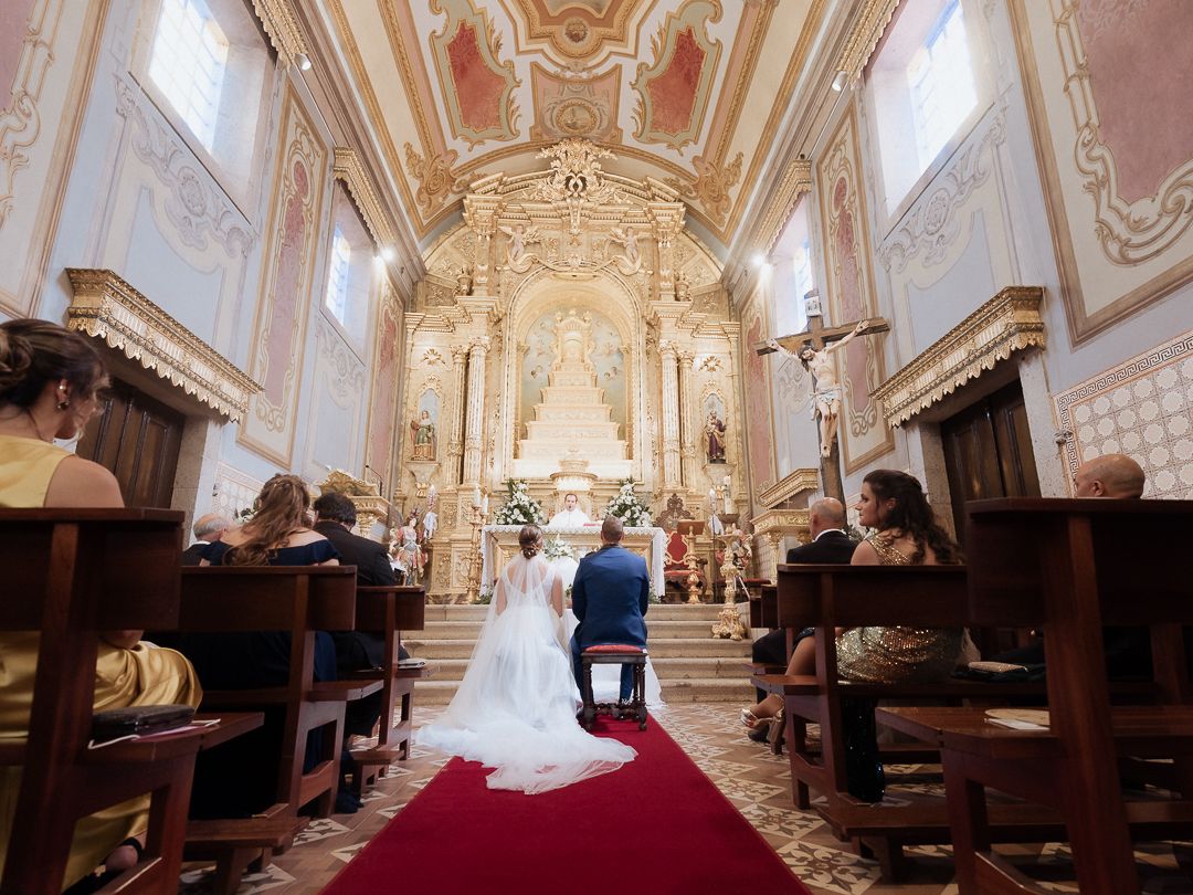 A couple celebrates their wedding ceremony inside an ornate baroque church with pink and white decorative interiors.