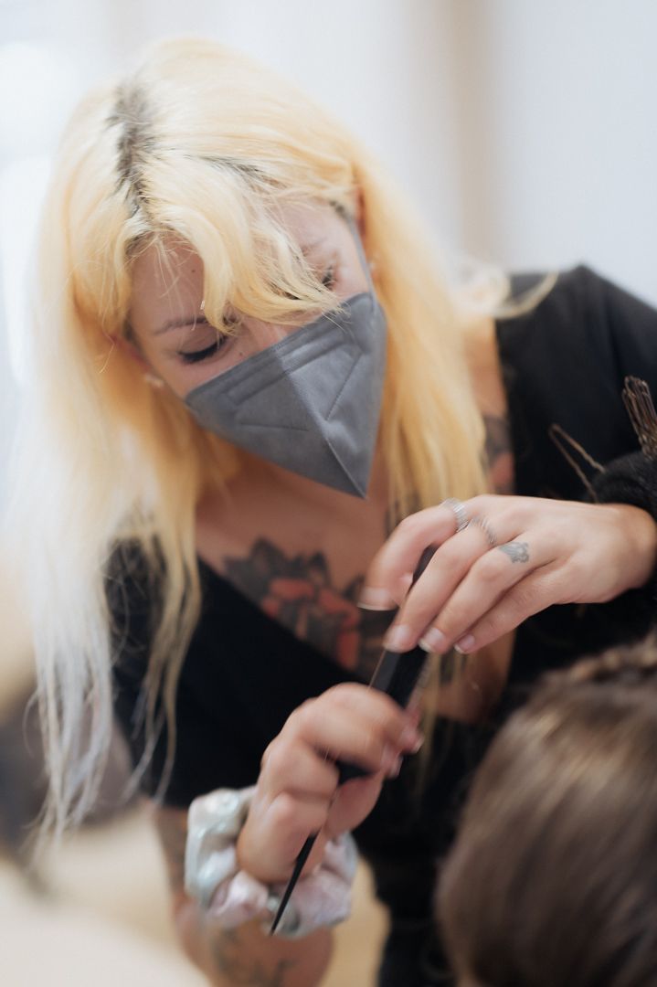 Hairstylist wearing protective face mask and black top working on client's hair in salon.