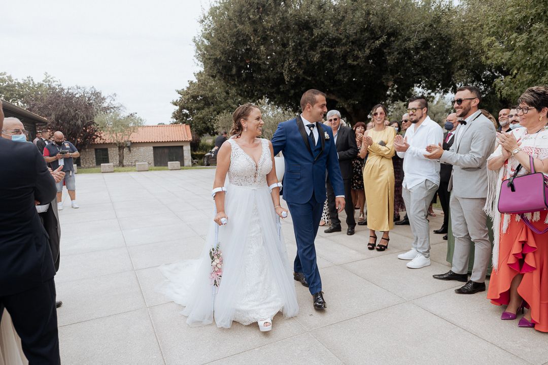 Wedding guests line up outside to watch a couple walk together during an outdoor celebration.