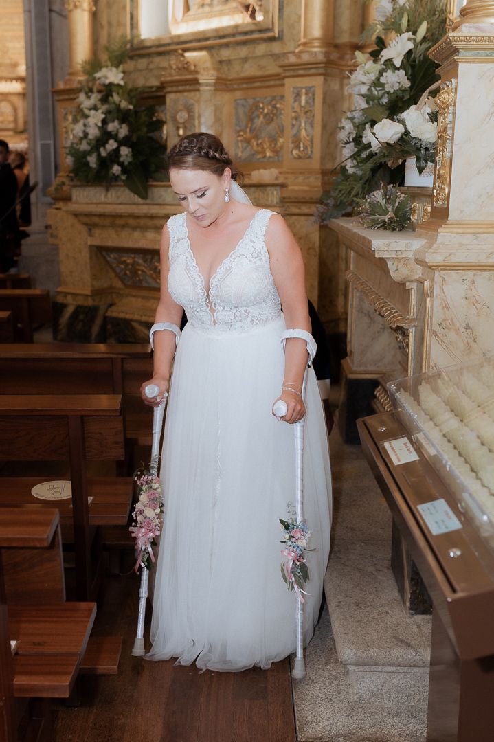 A bride in a flowing white tulle gown with lace details and plunging neckline stands in an ornate church interior.