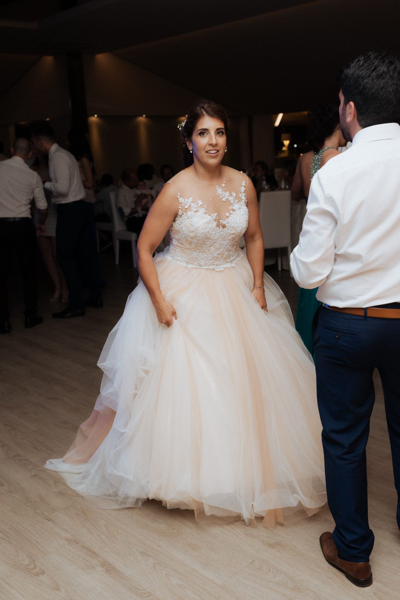 A person in a romantic tulle ball gown with lace bodice dances on a light wood floor at a wedding reception.