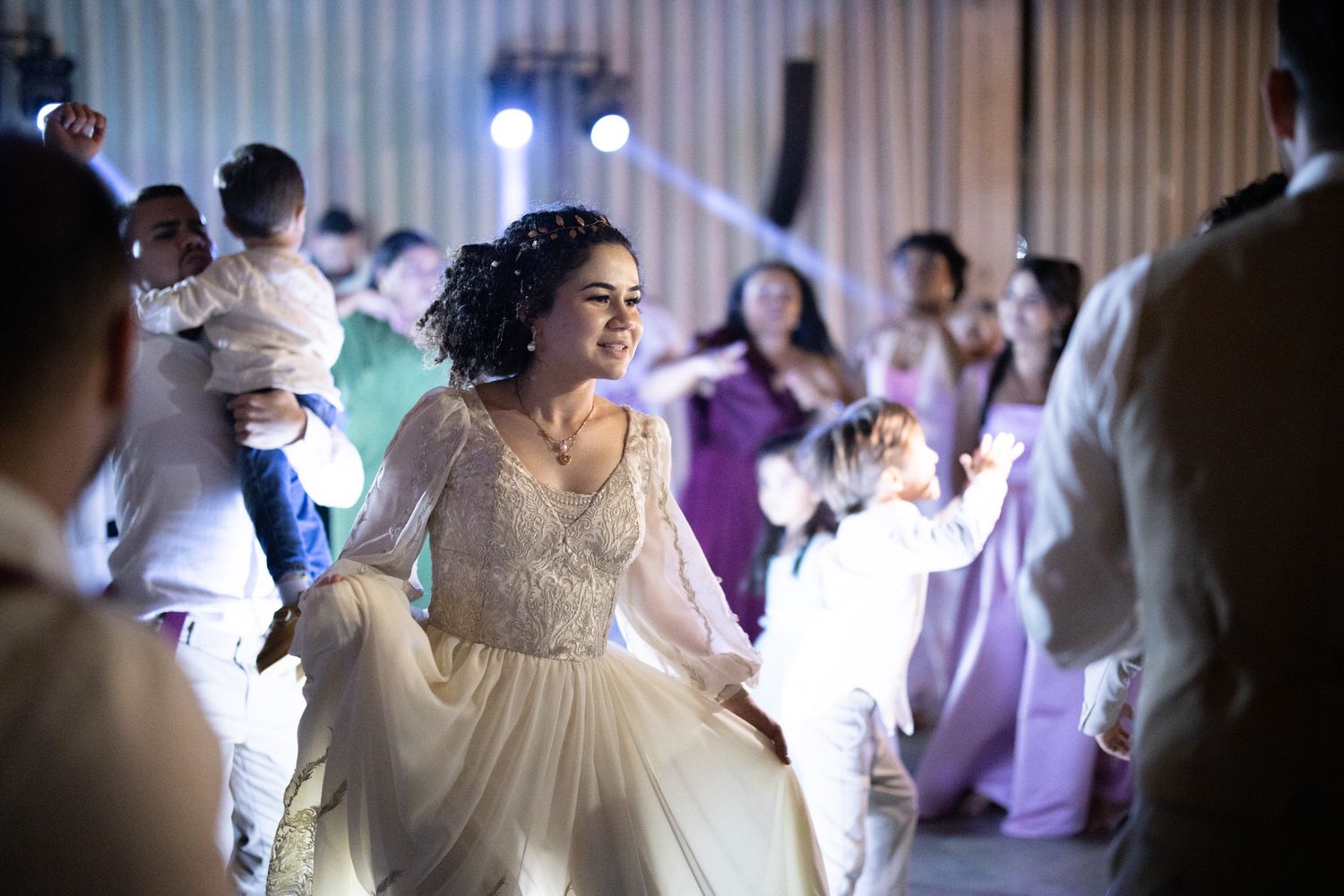 A bride in a flowing white gown twirls on the dance floor during a wedding reception as guests watch in the background.