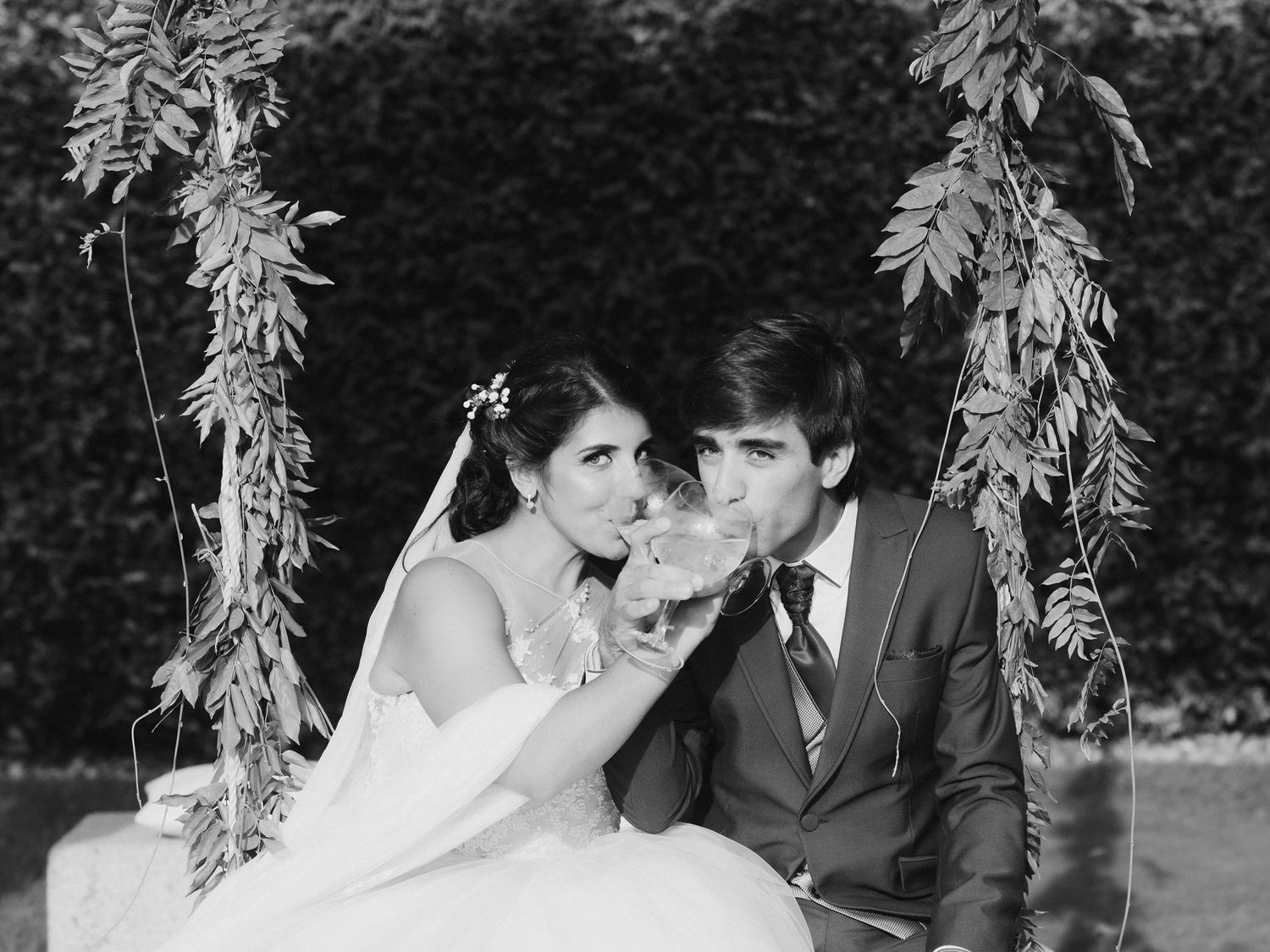 A romantic black and white photo shows newlyweds sharing a sweet moment on a floral-decorated garden swing.
