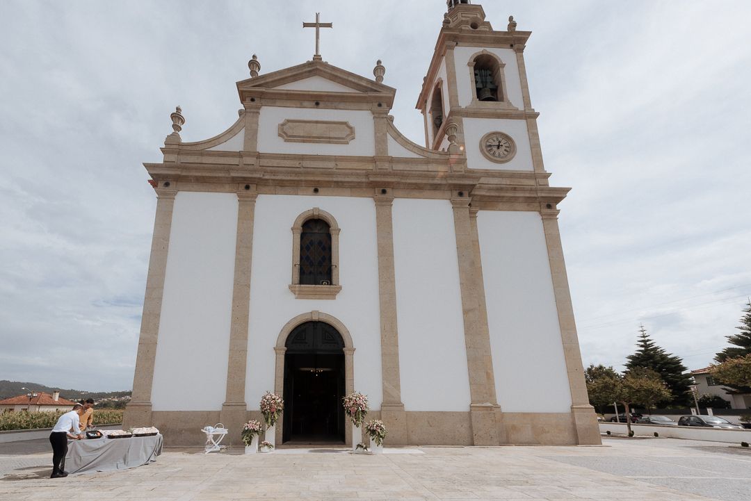 White Portuguese colonial church with bell tower and cross stands against cloudy sky in historic town square.