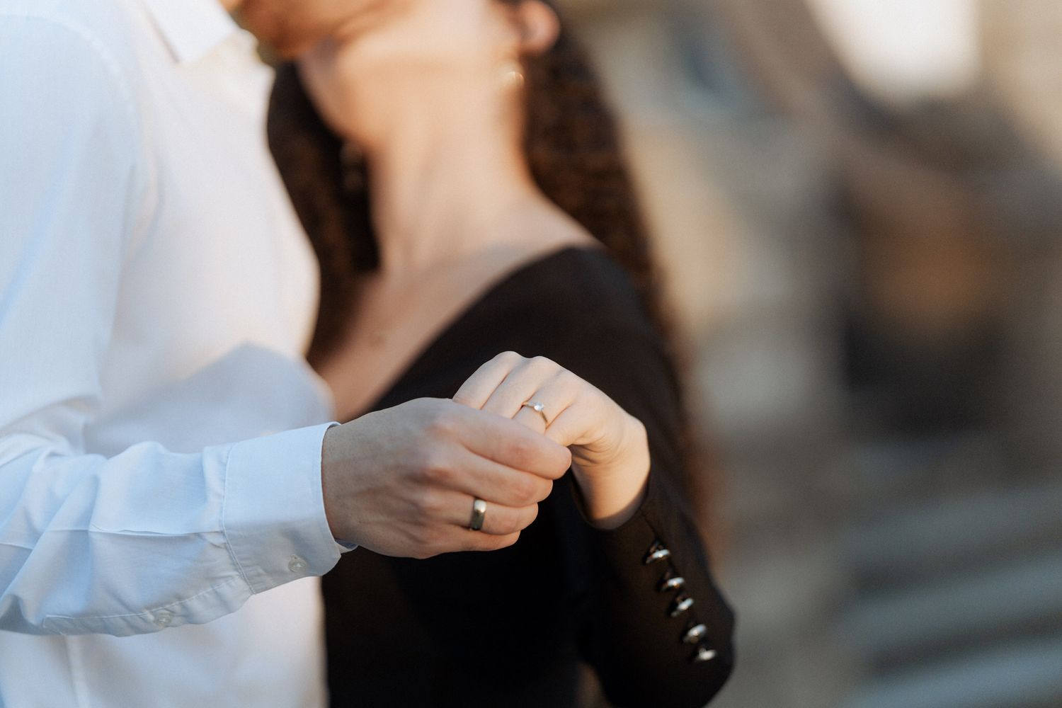 Close up of two people's hands touching gently, with one wearing an engagement ring on their finger.