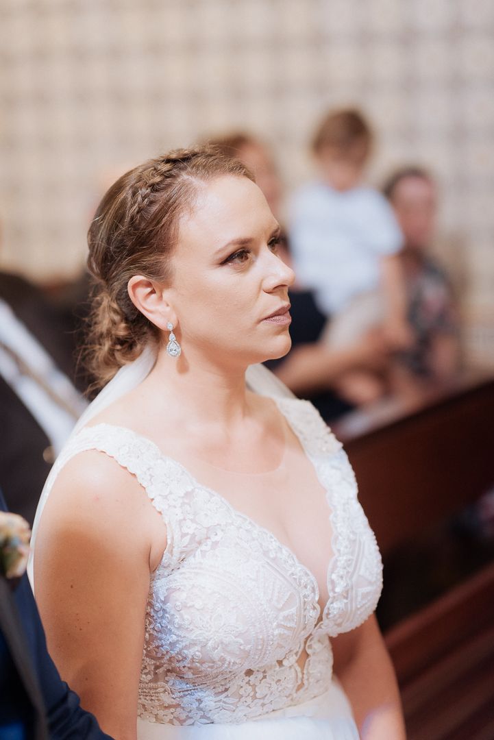 A person wearing an elegant white lace wedding dress stands in profile during a wedding ceremony.