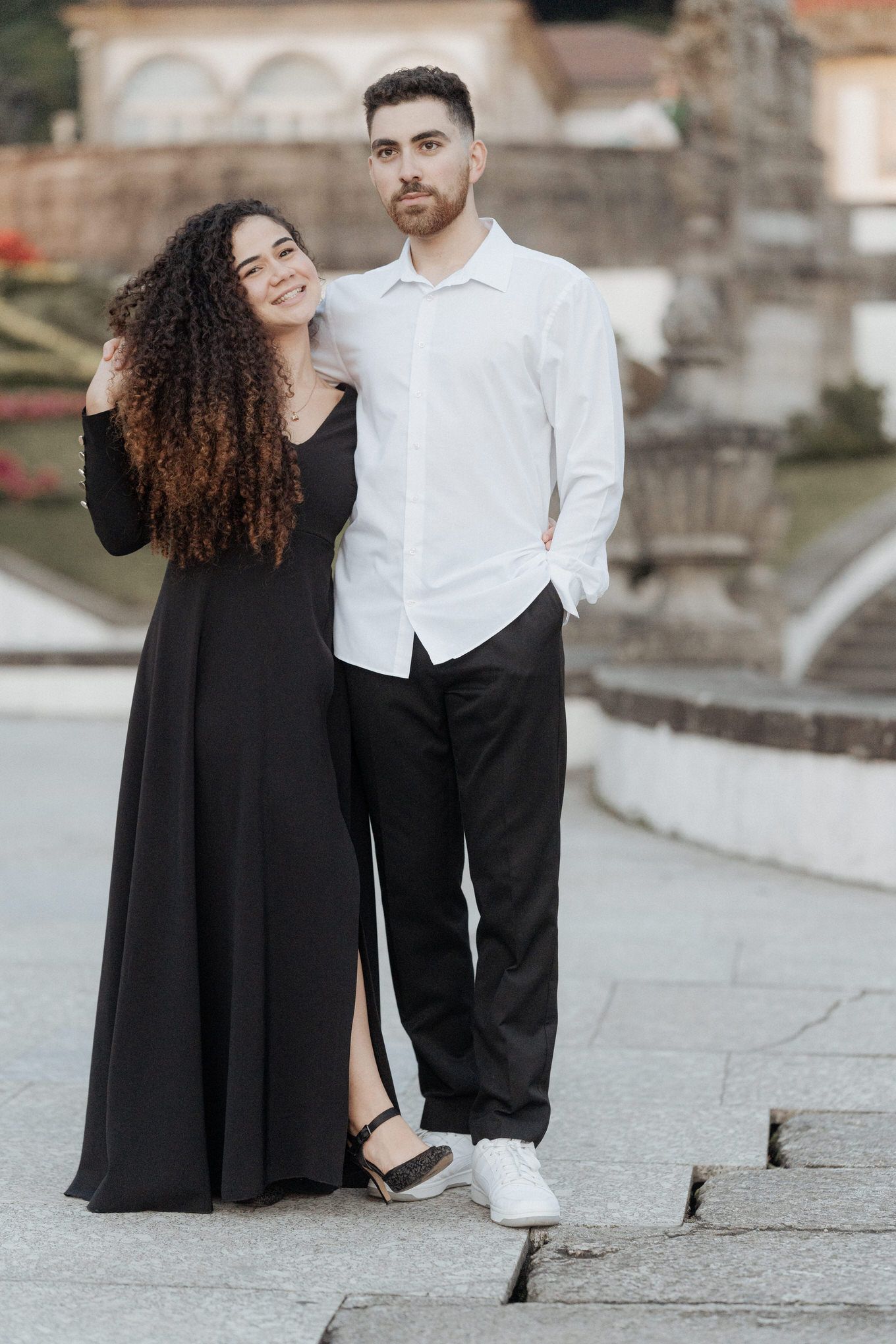 A couple in contrasting black and white outfits pose together on stone steps for a romantic photoshoot.