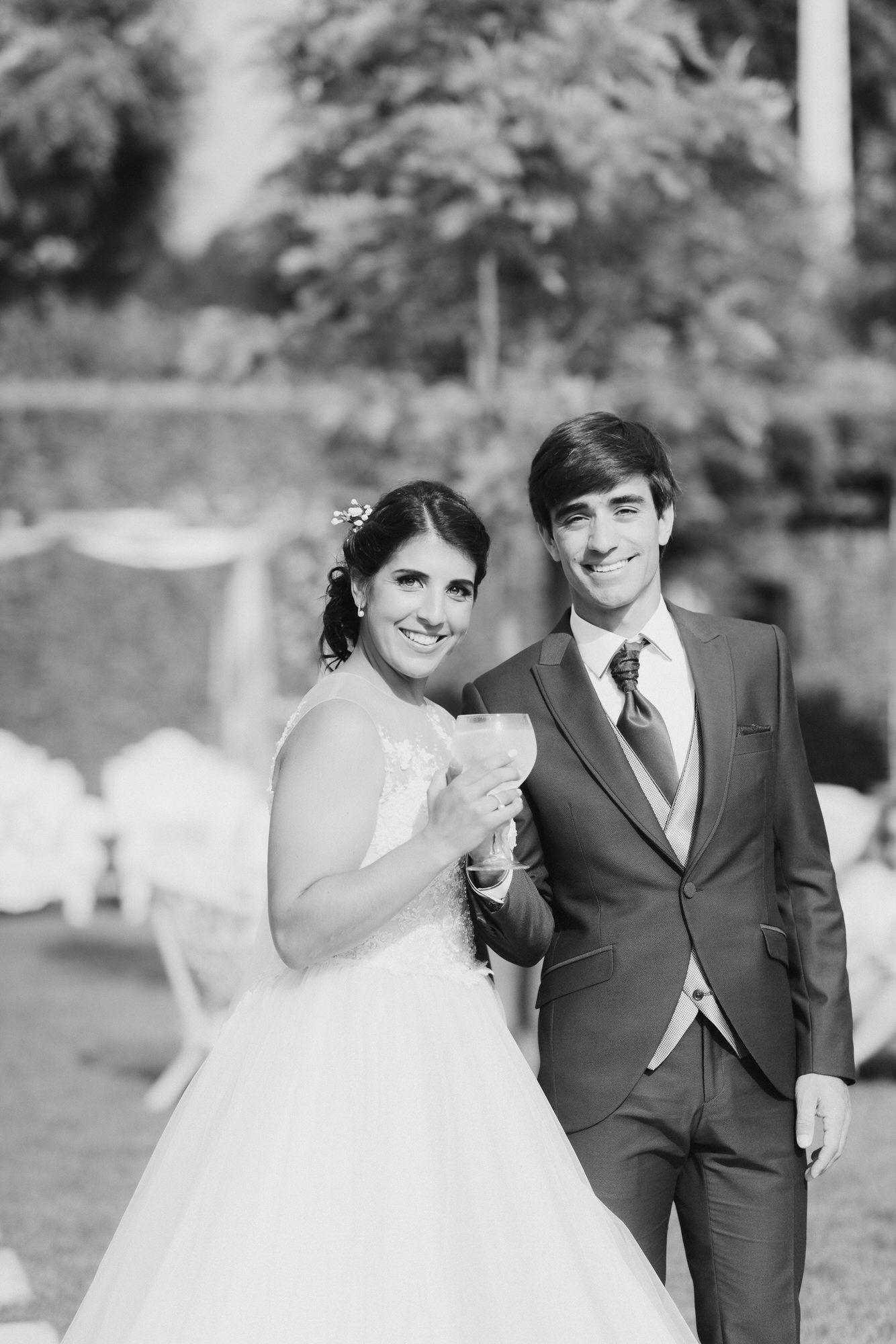 A joyful pair in wedding attire laugh and smile while walking together outdoors in a natural setting.