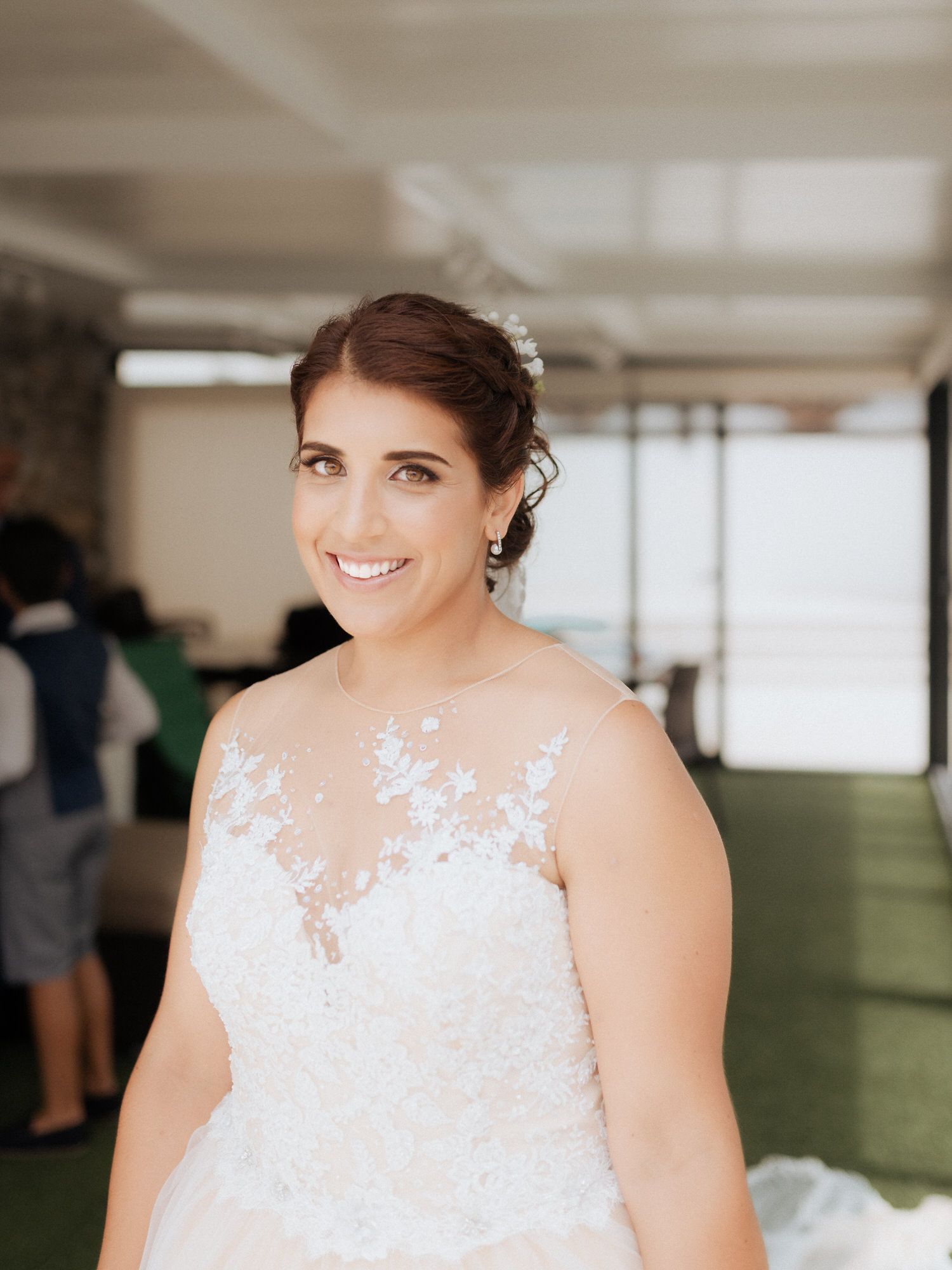 Bride in elegant lace white wedding dress poses for portraits in bright indoor venue.