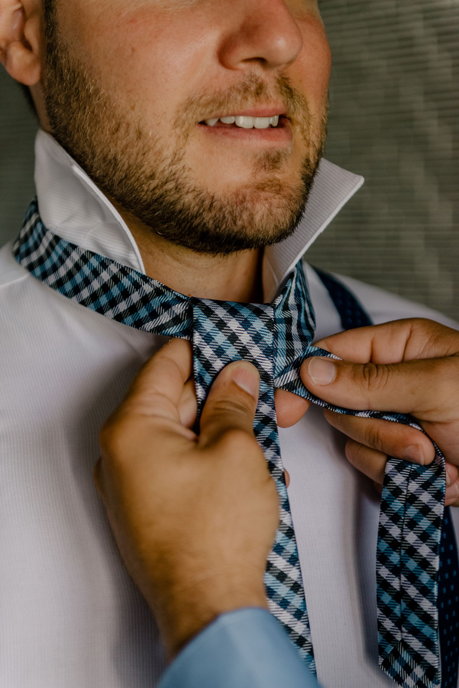 Detalhe de close-up do noivo e de mãos ajustando uma gravata borboleta xadrez em uma camisa branca. Fotografia de casamento.