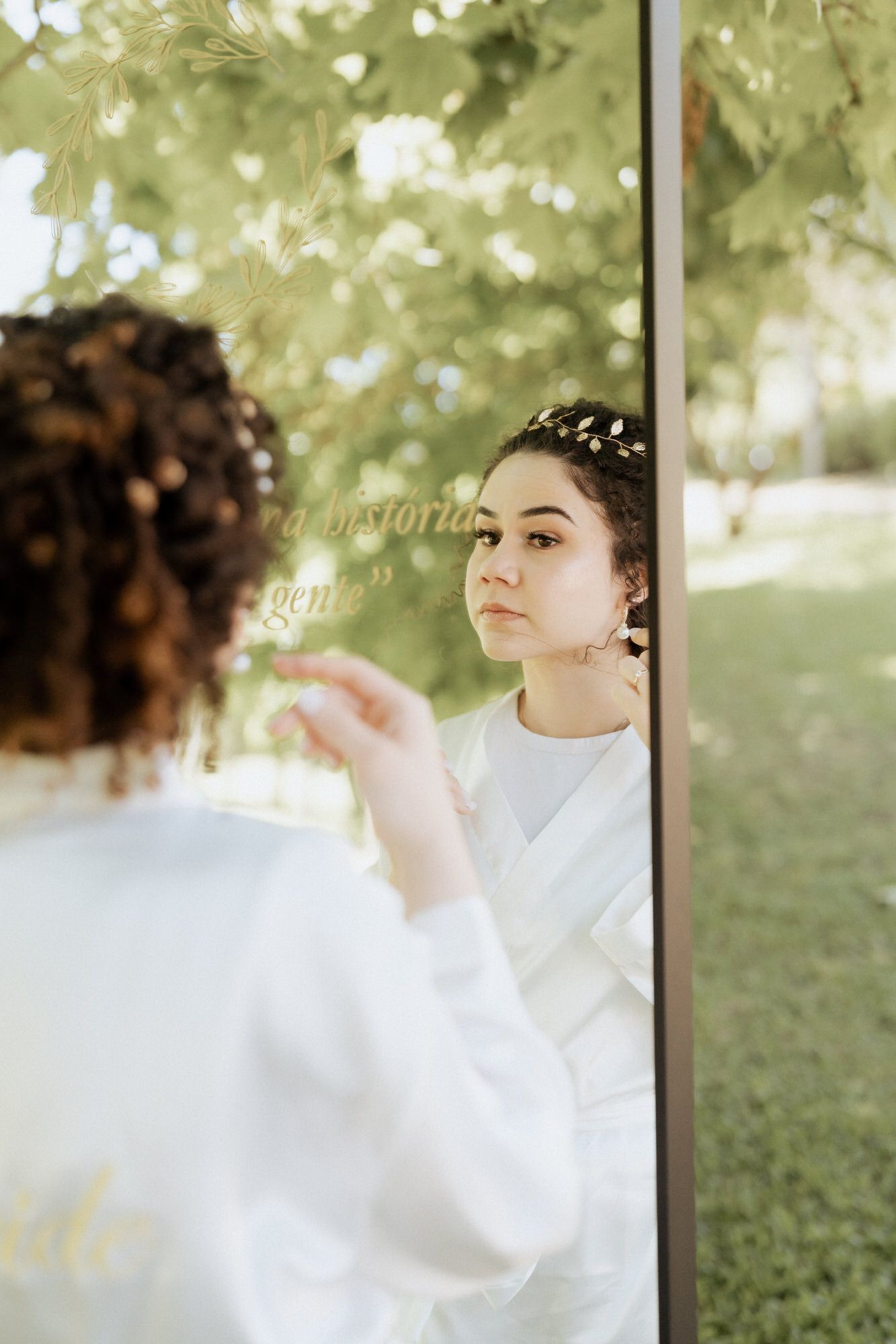 A serene reflection in a mirror outdoors shows white clothing and leafy greenery in the background.