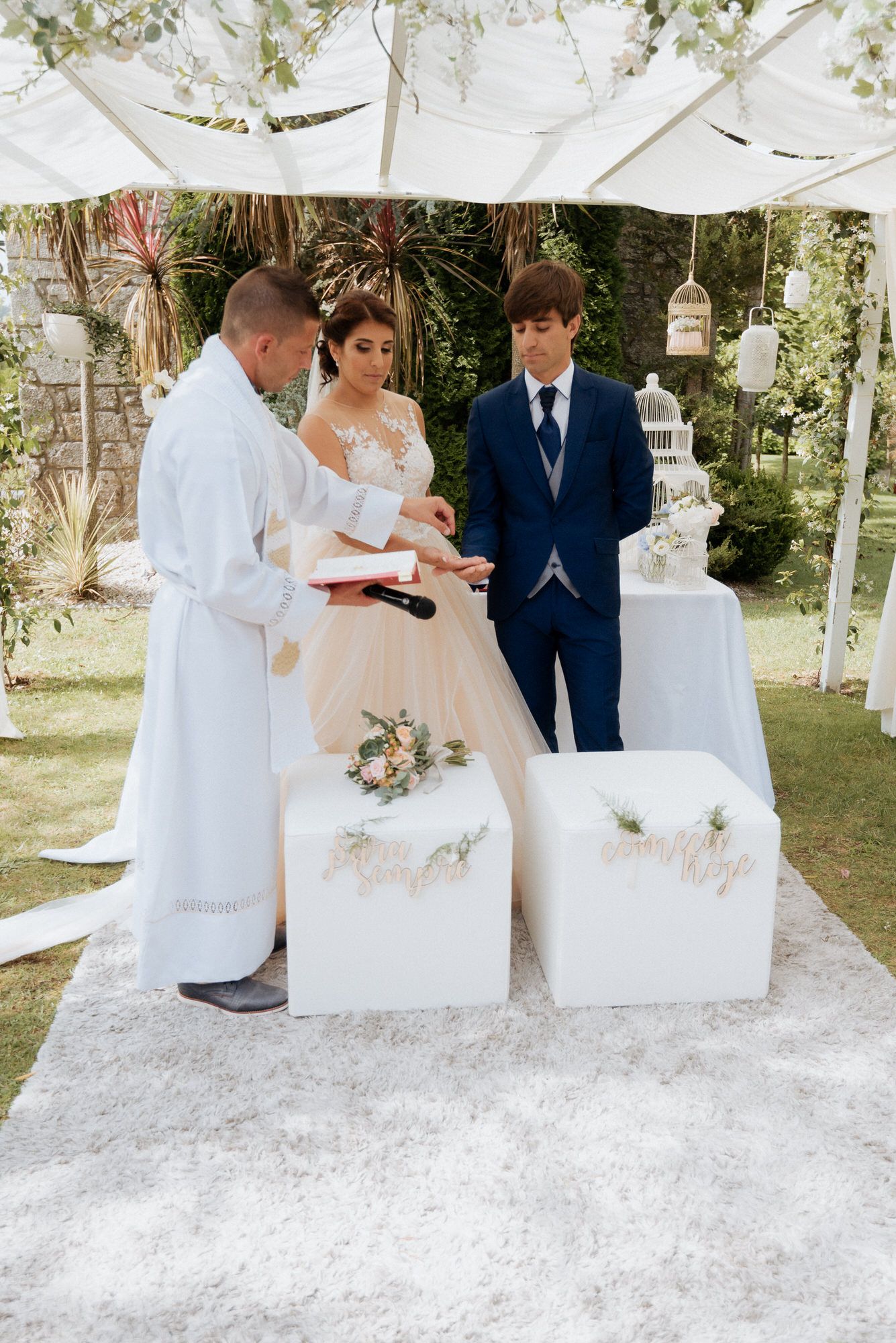Wedding ceremony outdoors with draped white fabric canopy and rustic seating arrangements in a garden setting.