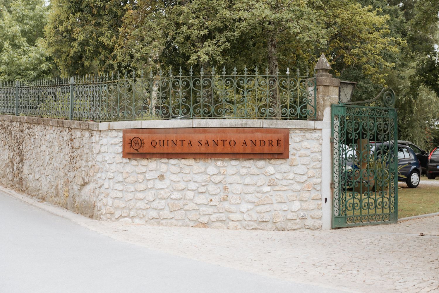 A stone wall entrance with wrought iron gates and a sign reading 'Quinta Santo Andre' in rustic style.