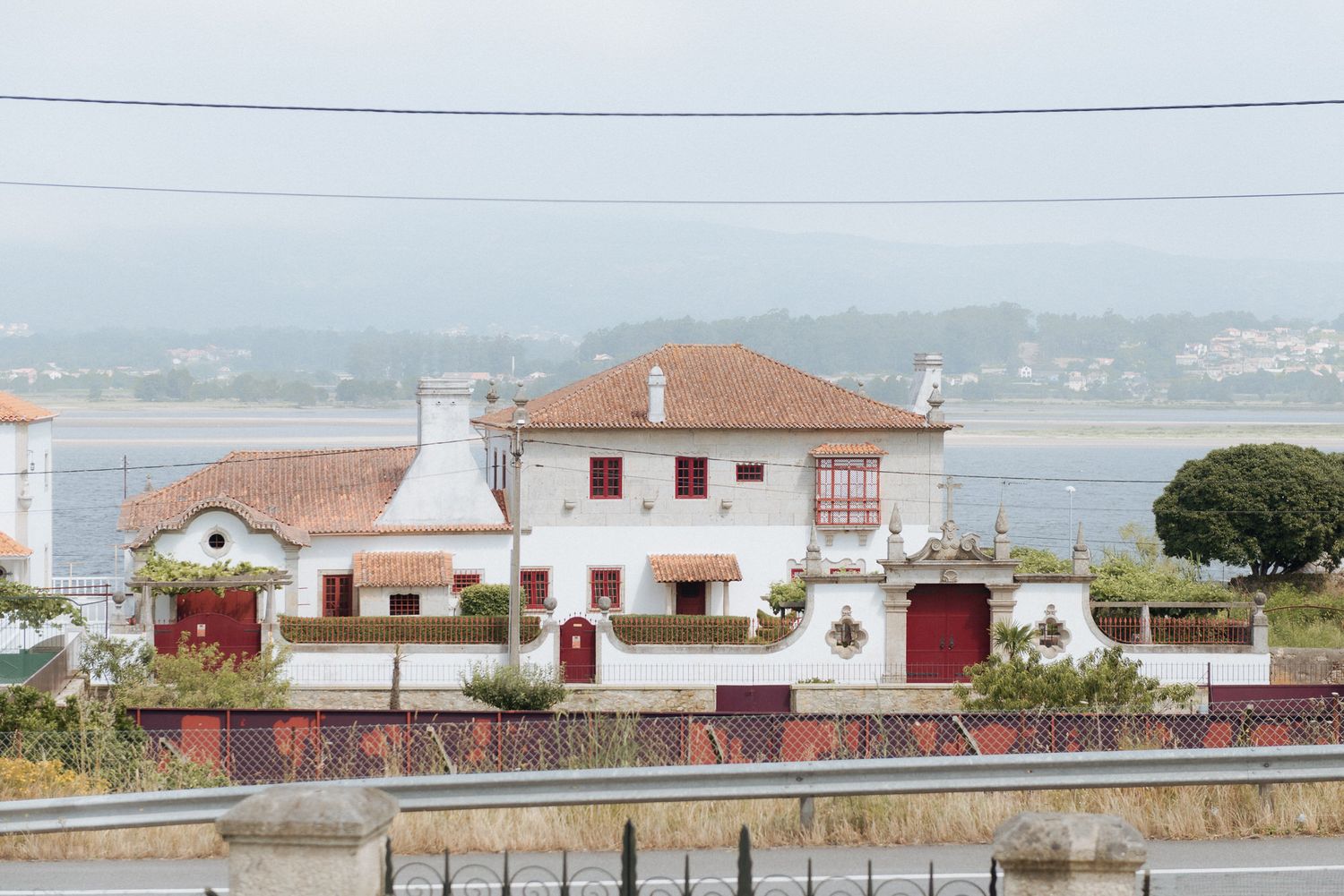 A white Mediterranean-style house with terracotta roof overlooks a coastal bay with power lines in the foreground.