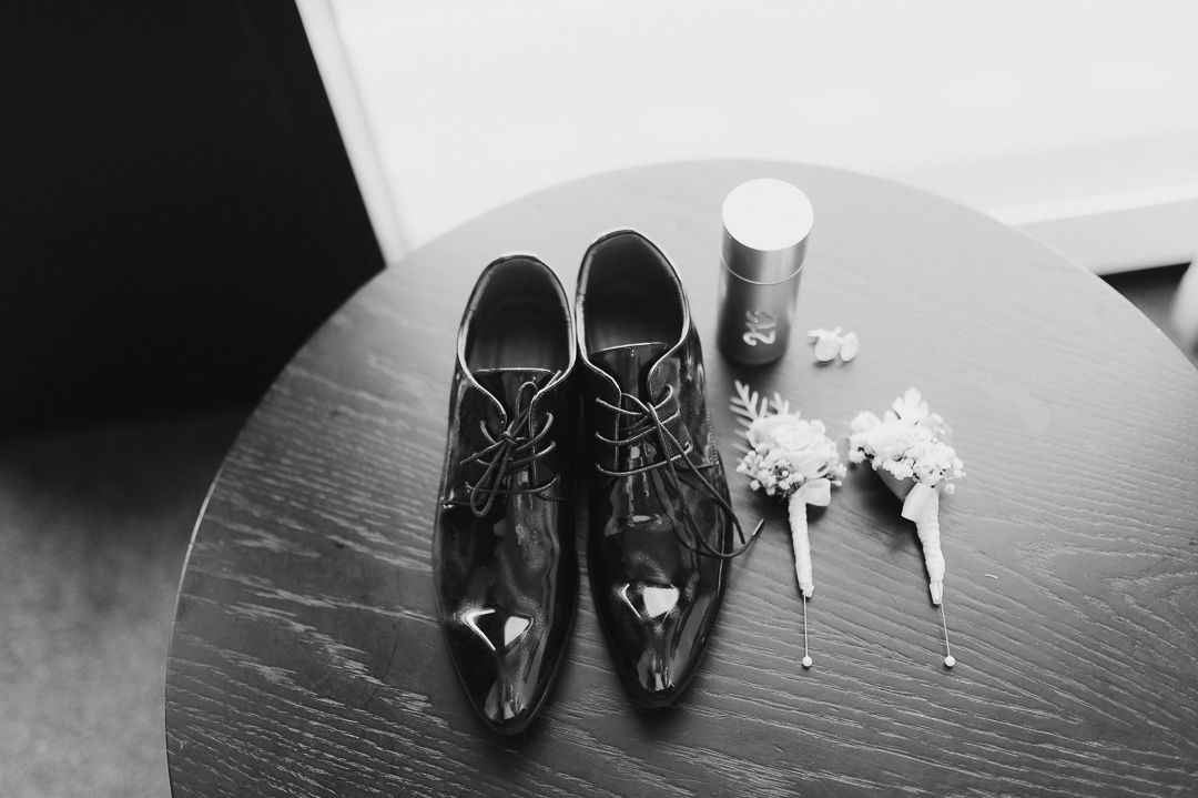 Black and white photograph of formal men's dress shoes and boutonnières on a wooden table.