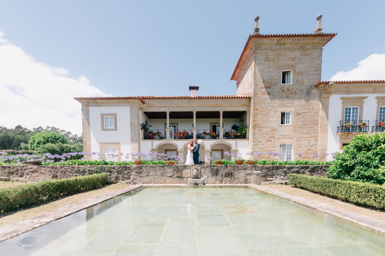 Elegante vila branca com fachada de pedra e piscina refletora em um jardim bem cuidado. Casamento Rústico.