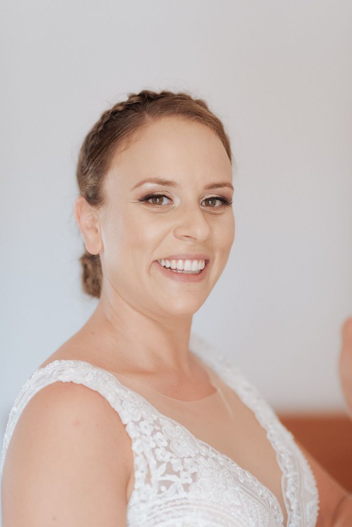 A radiant bride wearing a white lace wedding dress with a scoop neckline smiles at the camera.