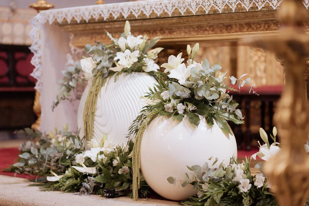 White pumpkin decorations adorned with eucalyptus leaves and white flowers create an elegant fall display at an event.