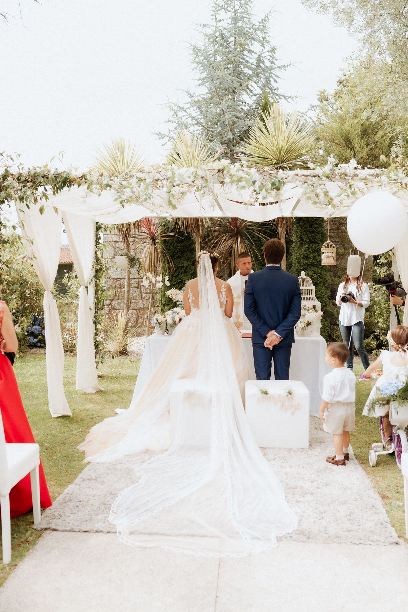 Elegant outdoor garden wedding ceremony with flowing white veil and draped fabric decor under a rustic wooden arch.