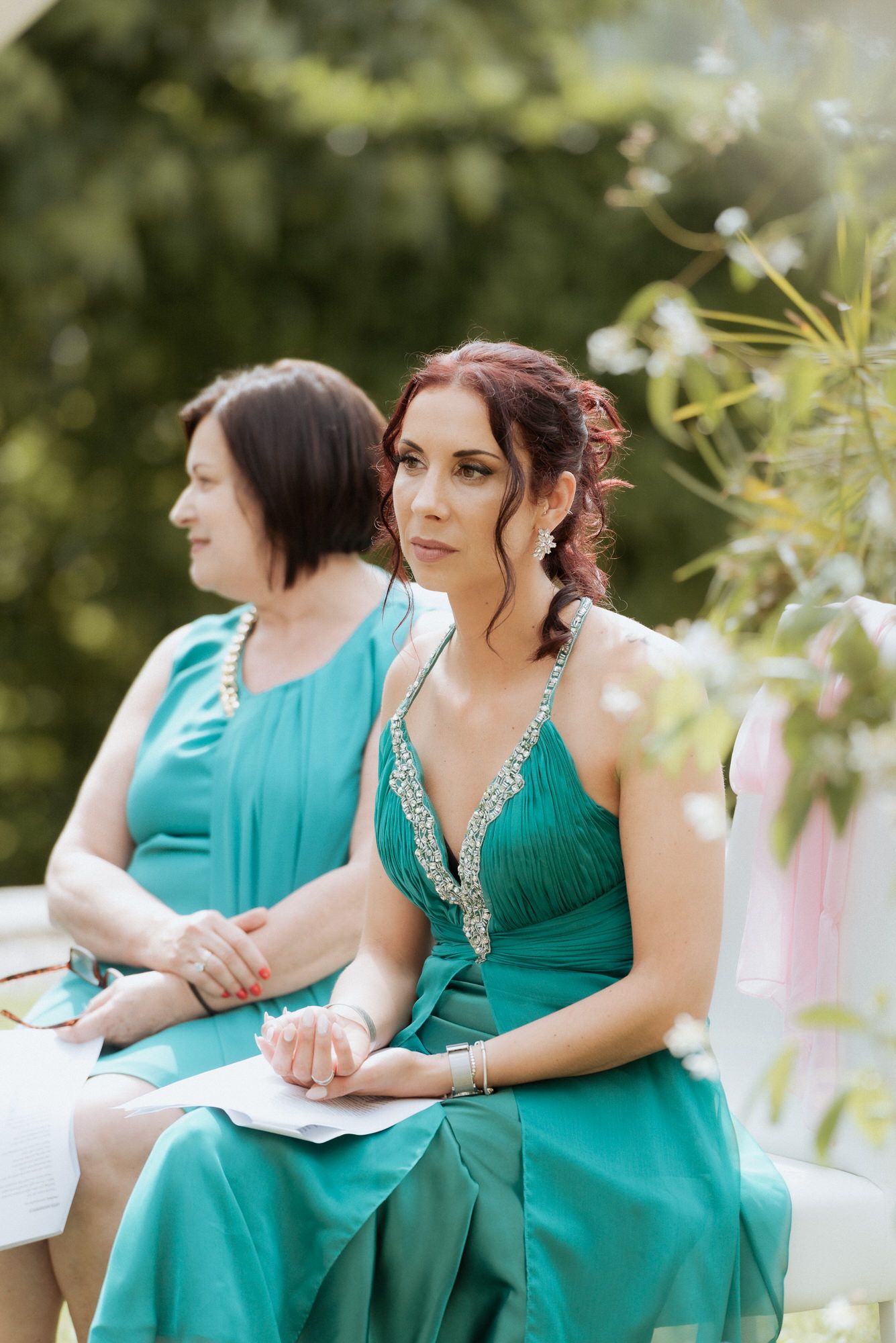 Wedding guests in formal attire seated outdoors with green garden background and soft lighting.
