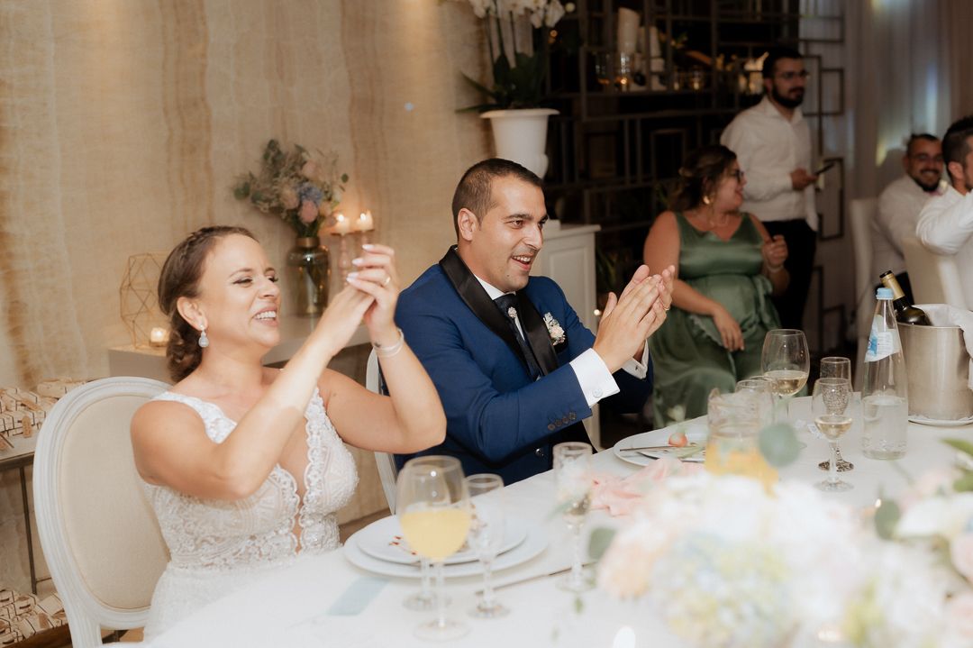 Newlywed couple at their wedding reception raising champagne glasses in celebration at an elegant table setting.