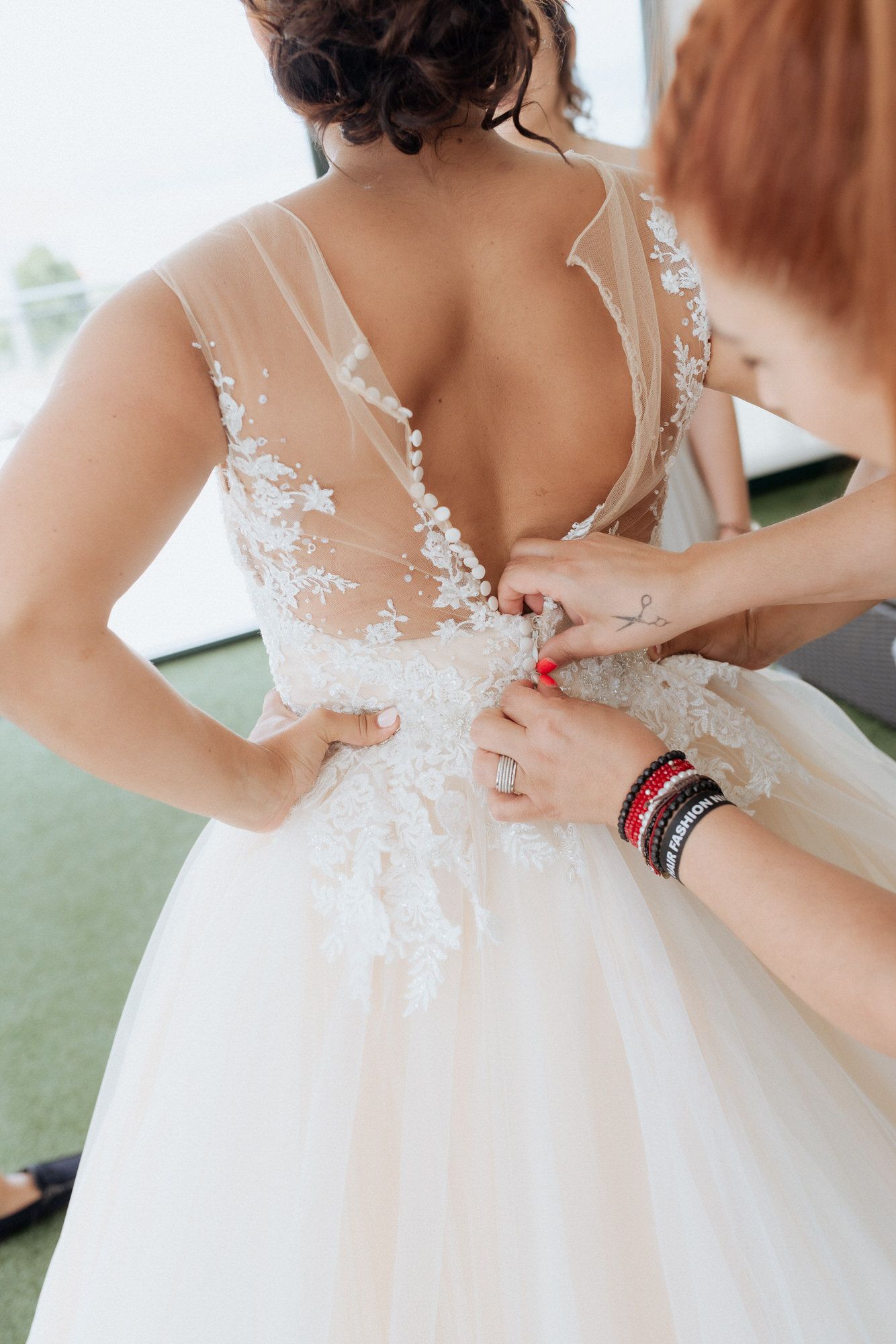 Wedding dress being fastened showing detailed lace overlay and sheer back with delicate floral appliques.