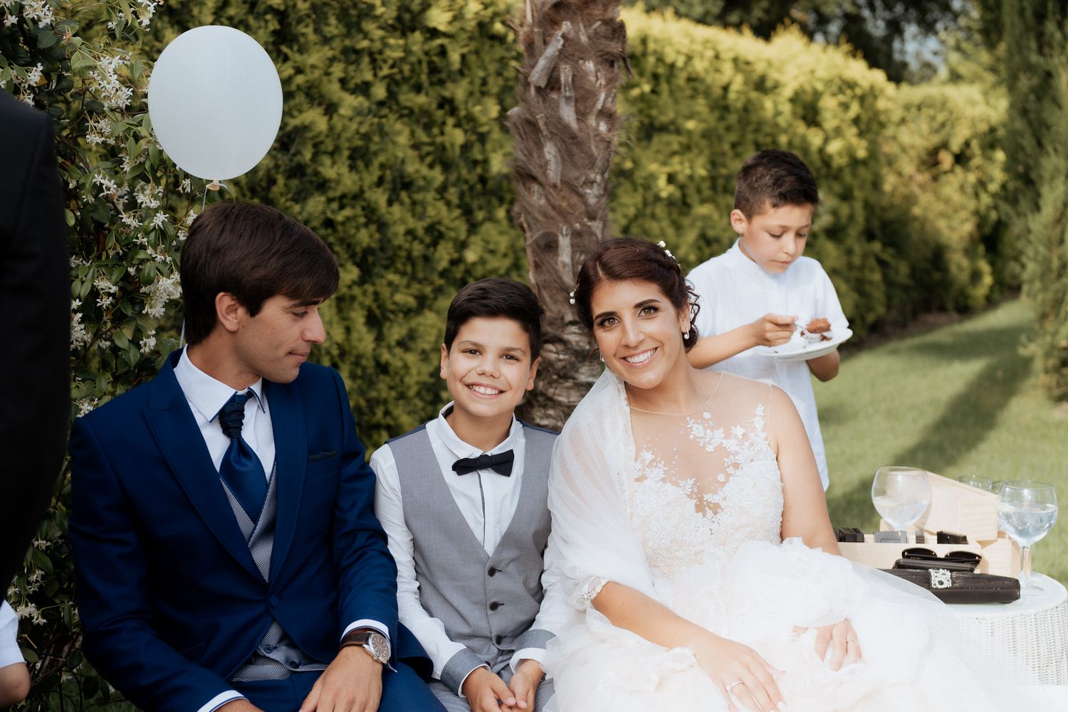 Wedding scene with a couple celebrating with children sitting on white chairs in a garden setting.