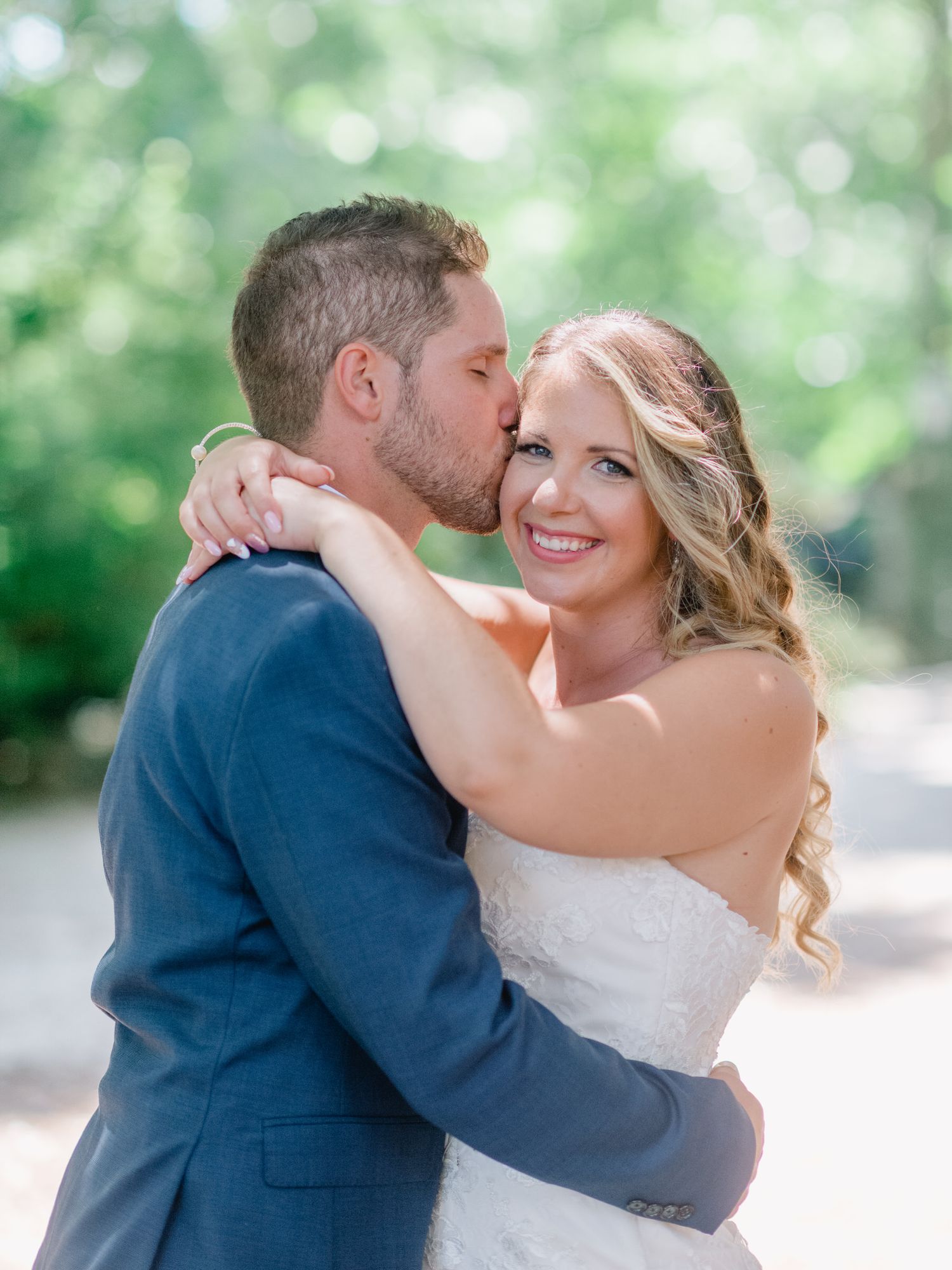 Intimate moment between newlyweds with soft bokeh background of green foliage.