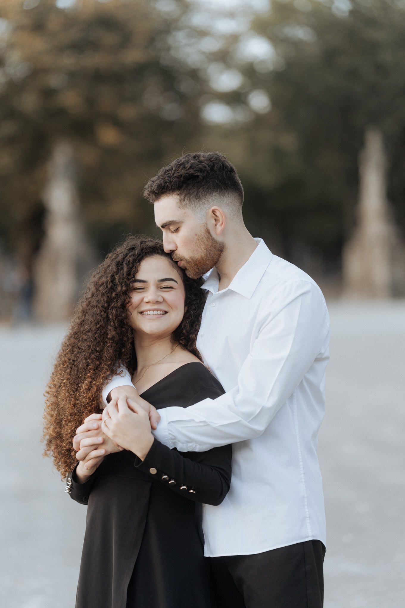 Um casal compartilha um momento de ternura enquanto se abraçam, ela vestindo preto e ele uma camisa branca.