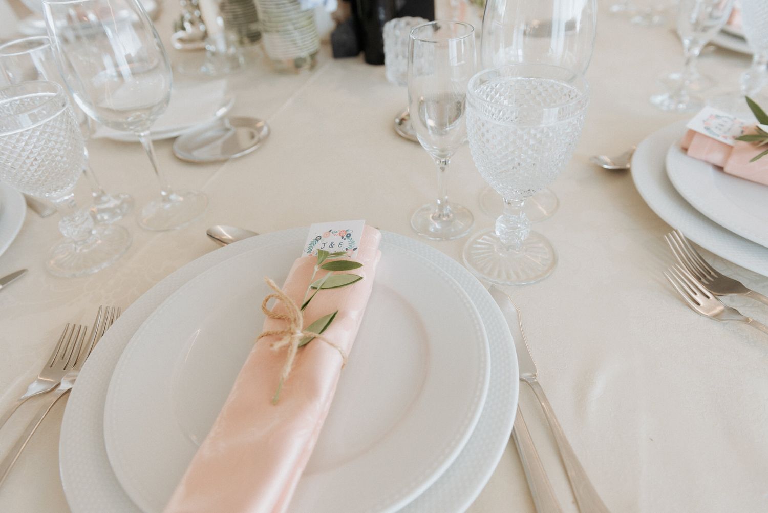 Elegant table setting with white plates, crystal glassware and peach napkins featuring a delicate bow at a formal event.