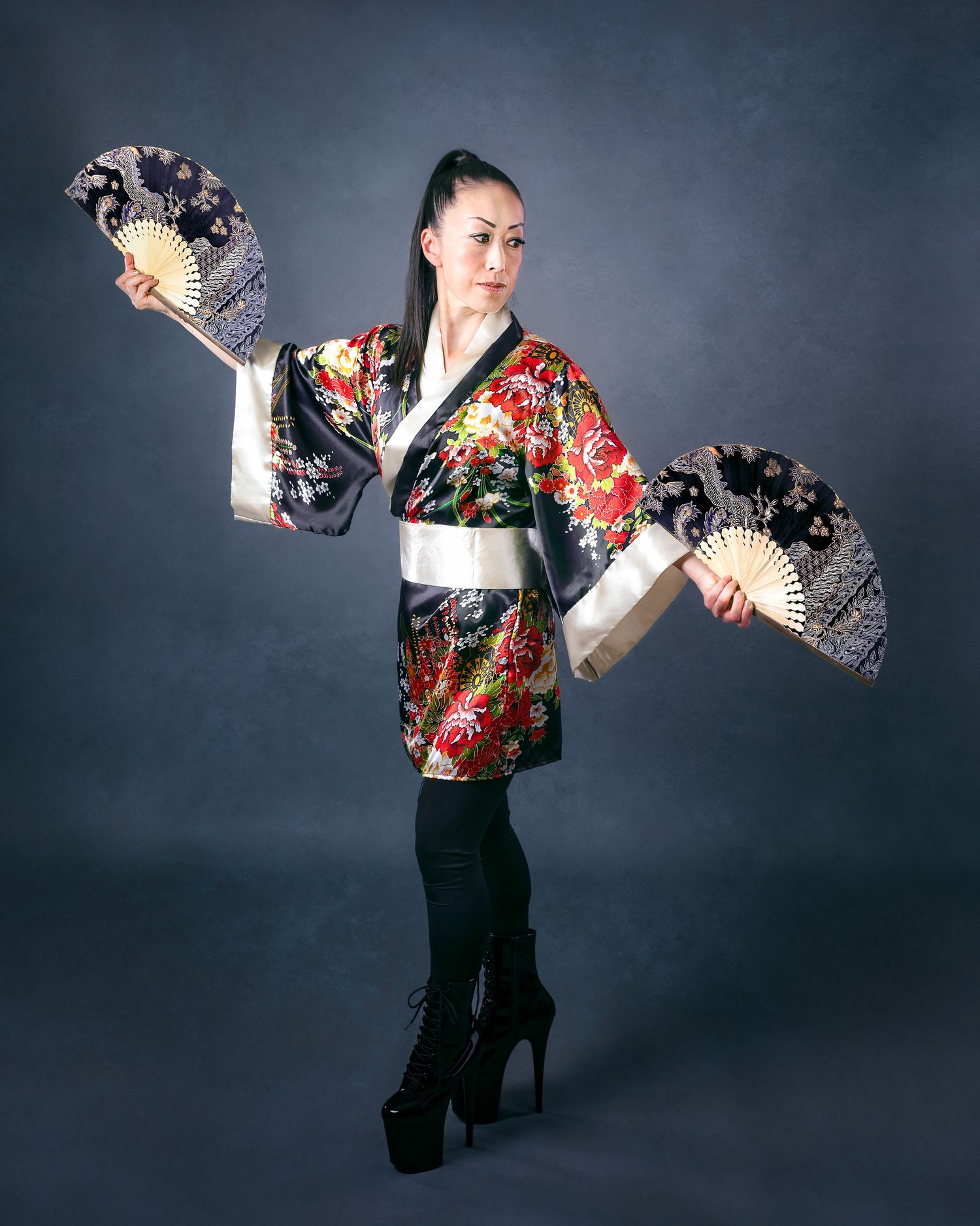 Figure in a vibrant floral kimono and black pants performs an elegant dance sequence against a dark backdrop.