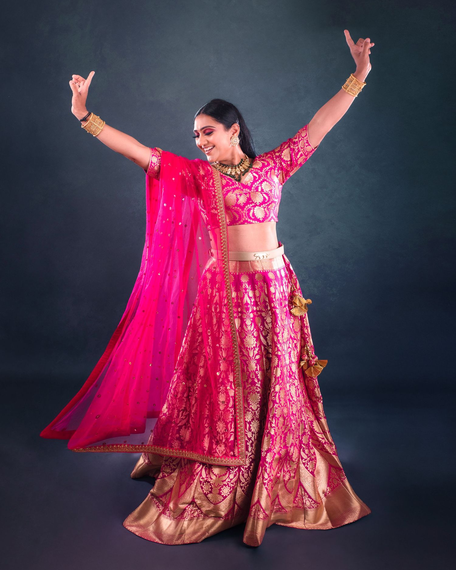 Traditional Indian dancer performs in vibrant pink lehenga with flowing dupatta against dark backdrop.