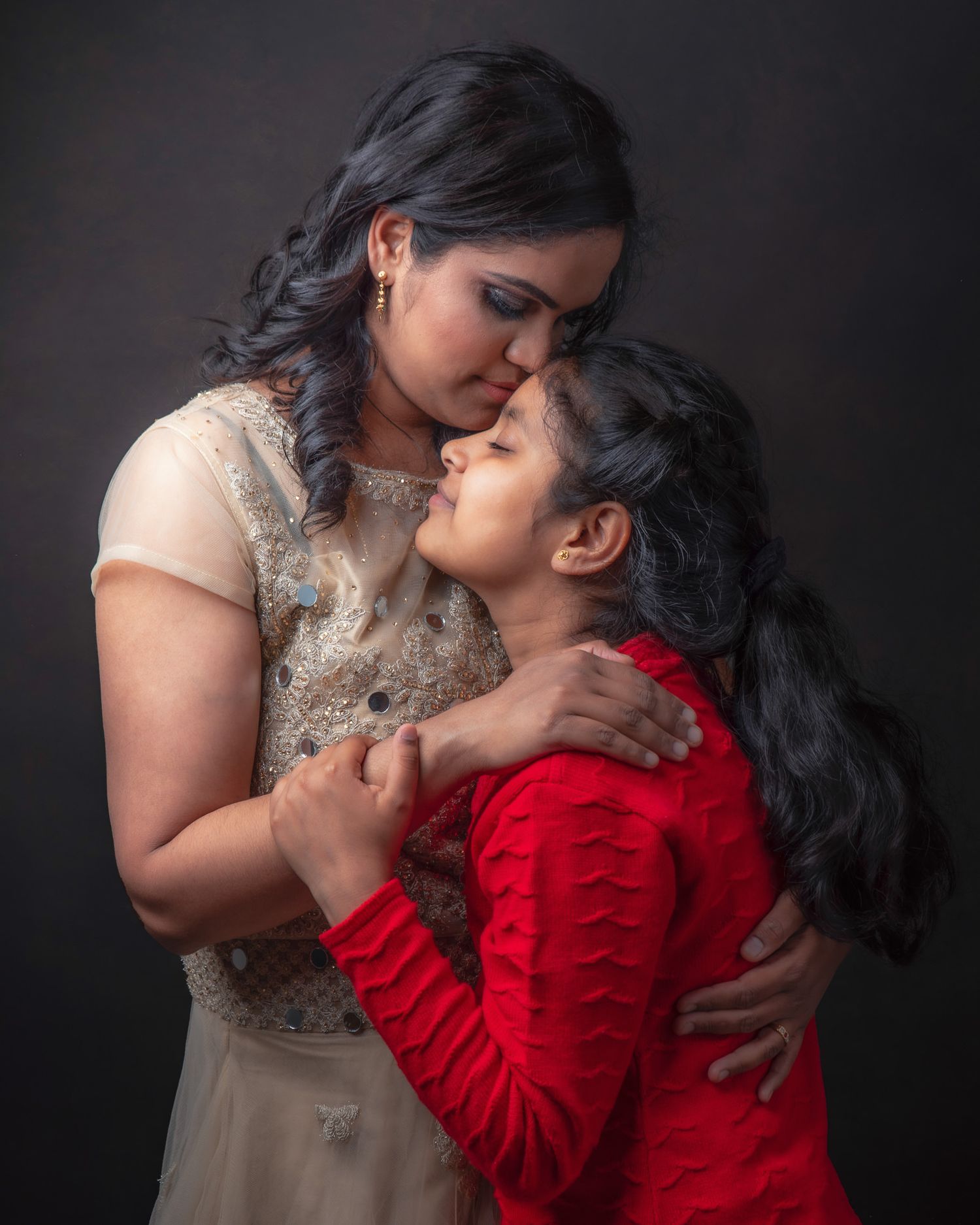 A tender embrace shared between two people wearing contrasting beige and red outfits against a dark background.
