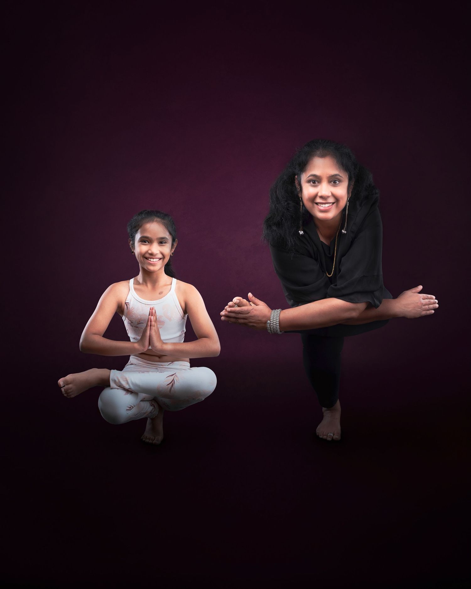 Two individuals in yoga poses against a dark purple backdrop, one seated in lotus pose and one in a standing pose.