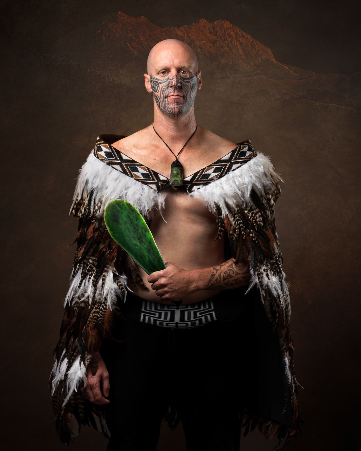 Artistic portrait of person wearing feathered cloak against dark background while holding large green leaf.