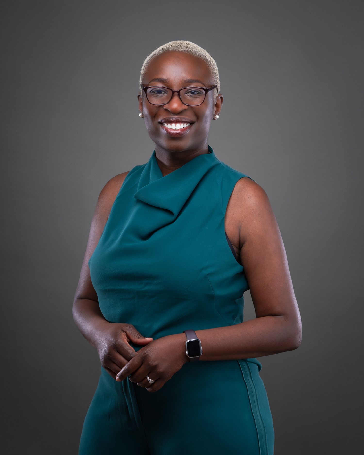 Professional portrait of someone in a teal sleeveless dress smiling warmly against a dark gray background.