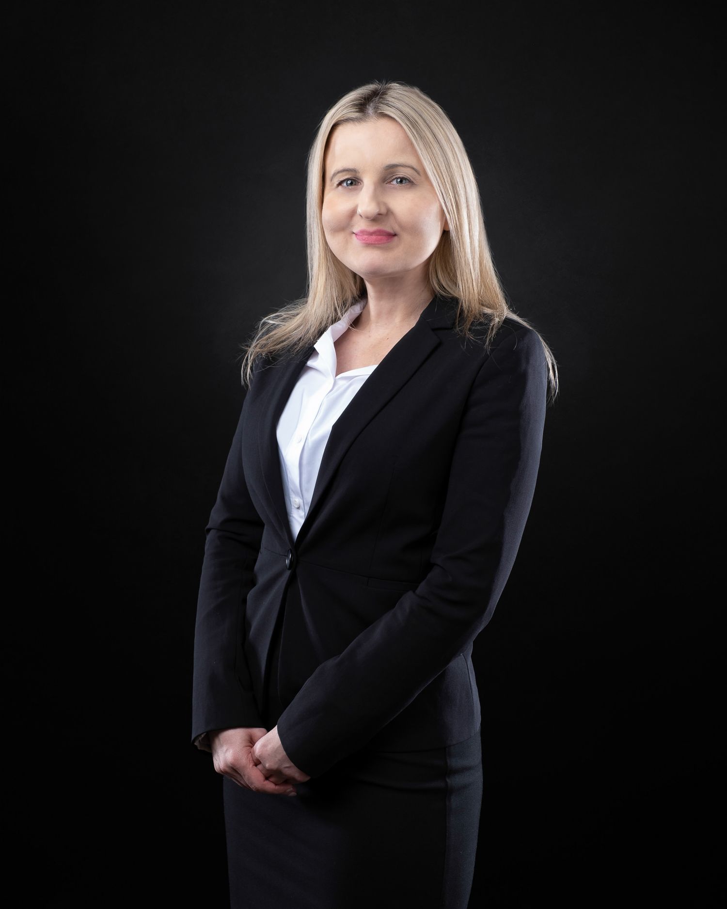 Professional studio portrait of a businesswoman in a black blazer and white blouse against a dark background.