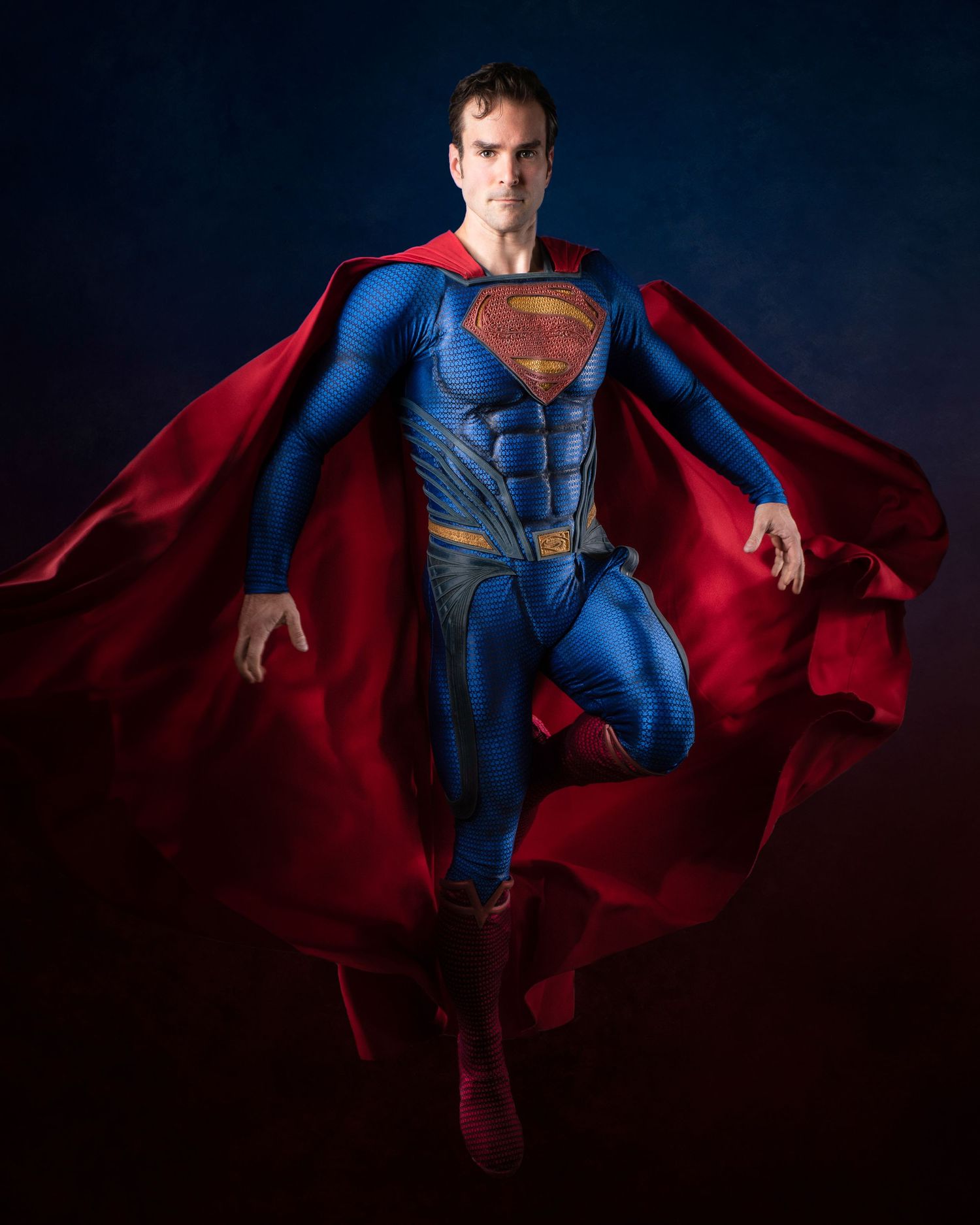 A performer in a Superman costume floats dramatically against a dark background with billowing red cape.