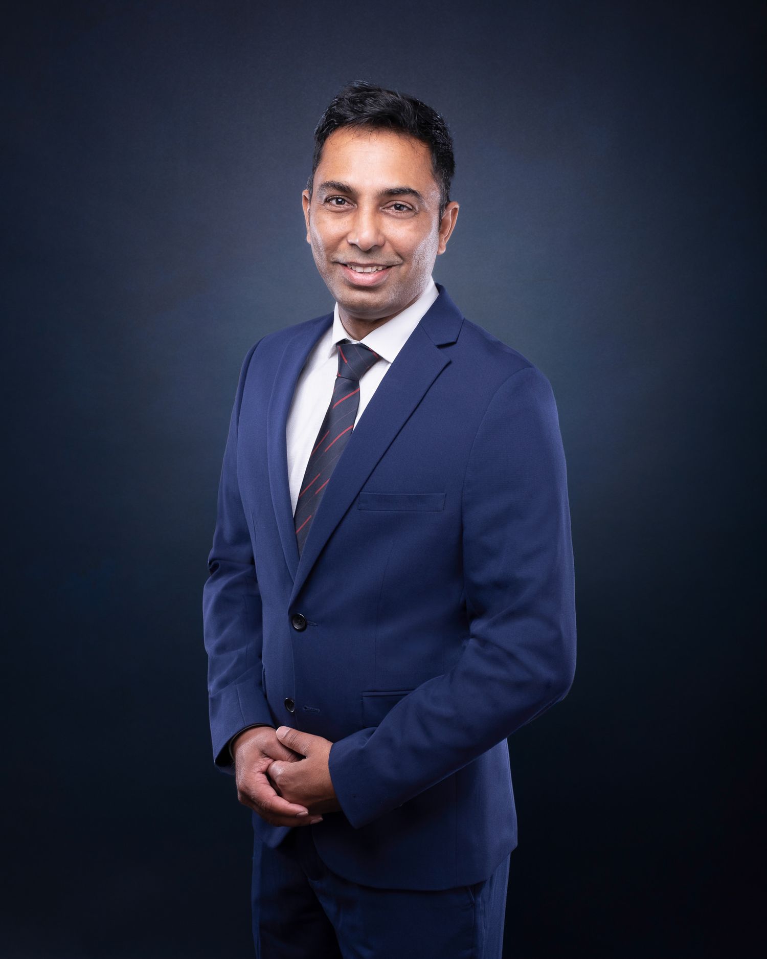 Professional business portrait of someone in a navy blue suit and dark tie against a deep gray background.